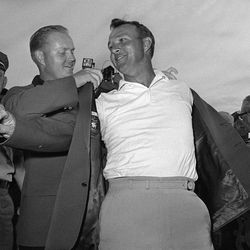FILE - In this April 12, 1964 file photo, Arnold Palmer, right, slips into his green jacket with help from Jack Nicklaus after winning the Masters golf championship, in Augusta, Ga. Palmer, who made golf popular for the masses with his hard-charging style, incomparable charisma and a personal touch that made him known throughout the golf world as "The King," died Sunday, Sept. 25, 2016, in Pittsburgh. He was 87. 