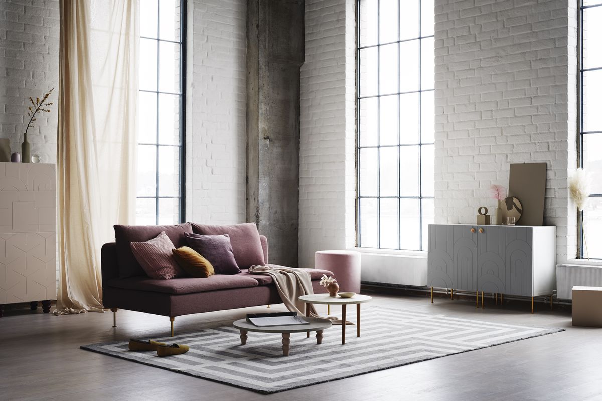 A living room has a rose colored couch, coffee tables, and large windows in a loft-like space. 