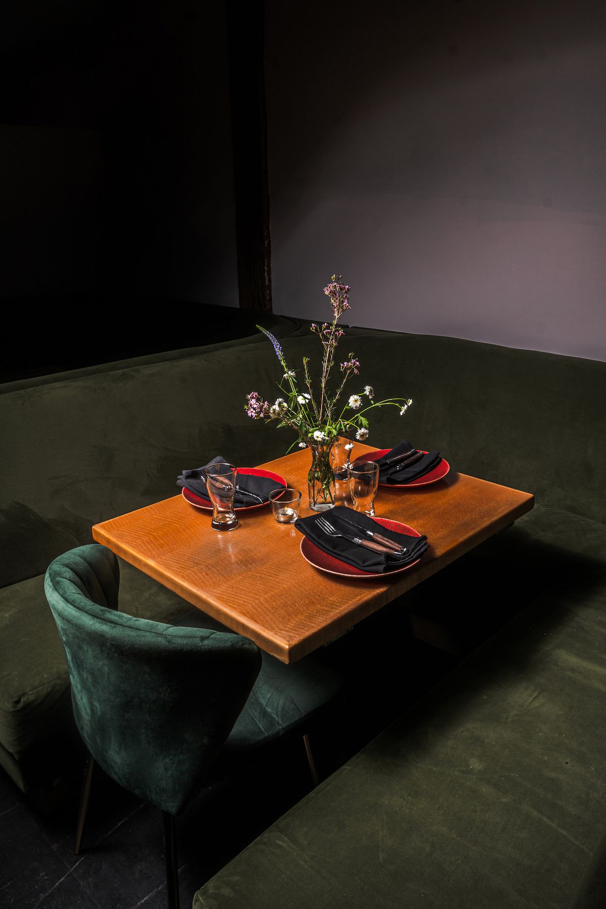 Three black and red settings inside a dark dining room on a wooden table.
