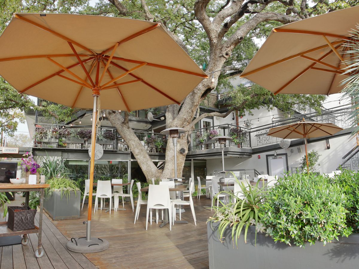 A restaurant patio with large umbrellas and a tree. 