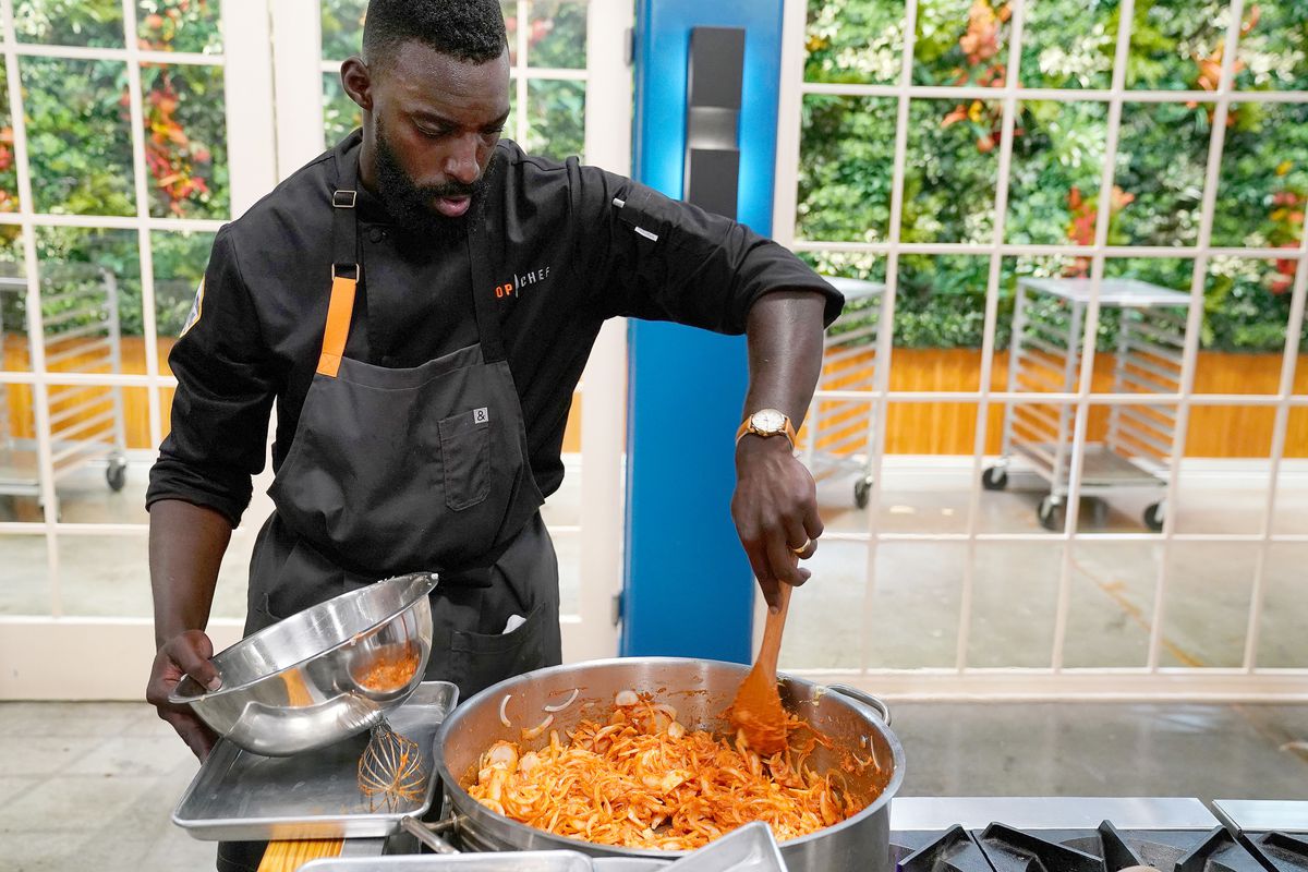 Top Chef all-star contestant Eric Adjepong focuses intensely on stirring a bright orange dish on a stovetop.