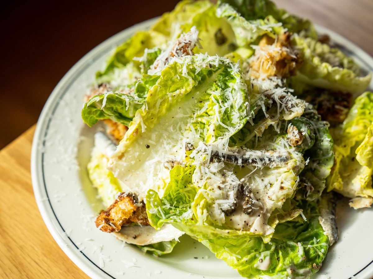 A plate of romaine lettuce covered in croutons, anchovy dressing, and cheese.