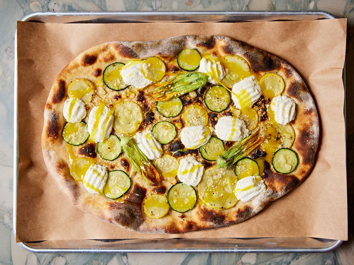 An overhead photograph of a pizza topped with slice squashed, mozzarella, and olive oil.