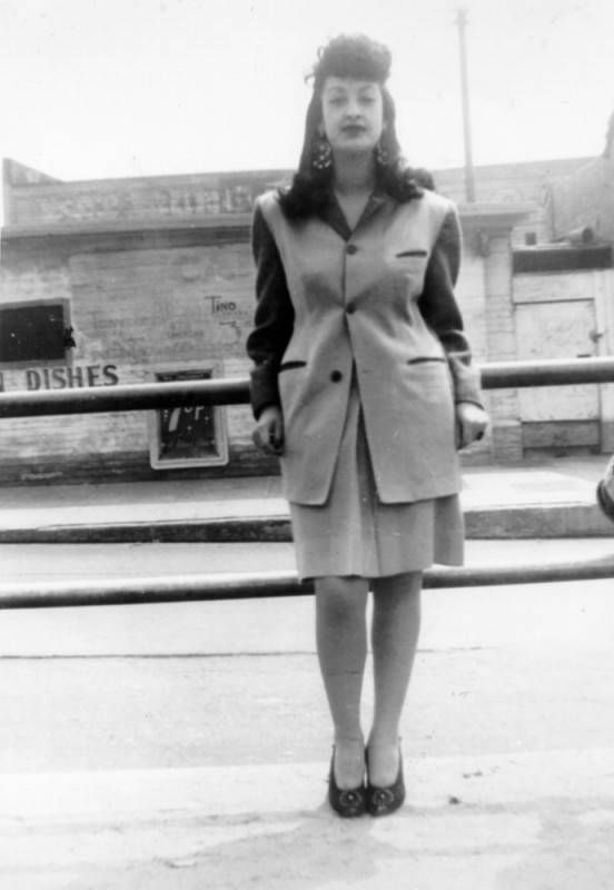 A black and white image of a young women in an oversized, single-breasted blazer, knee-length pencil skirt, and pumps.