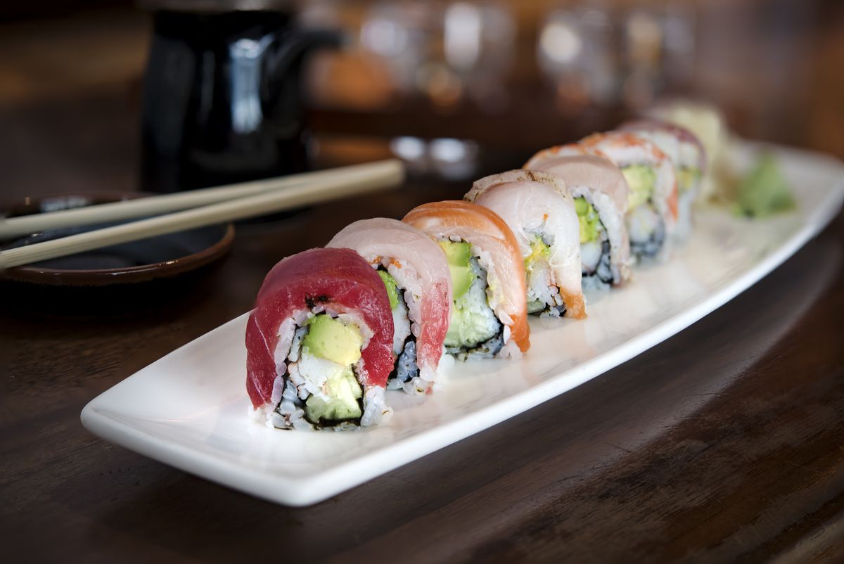 A sushi roll is elegantly displayed on a white rectangular plate, with each piece topped with a different fish, including shrimp and salmon.