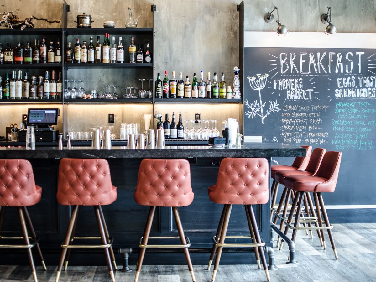 Pale red bar stools line an L-shaped bar, with a chalkboard wall displaying menu items off to the right