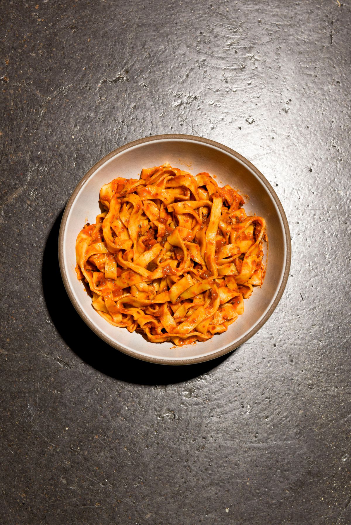 Fresh tagliatelle with nduja bolognese sauce on a white plate.