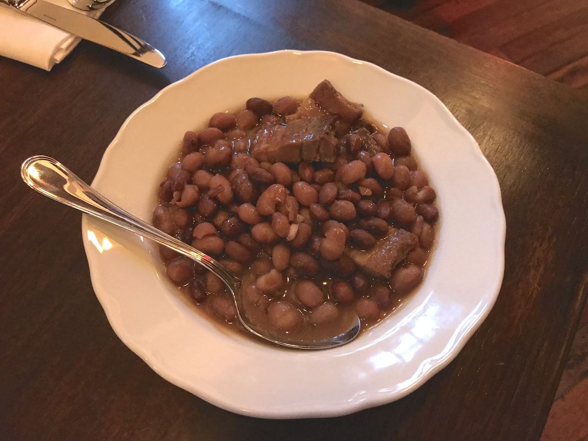 A white bowl with brown beans and pork belly.
