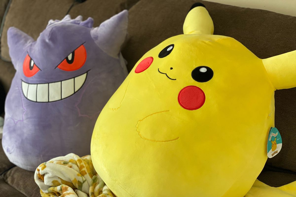 A Pikachu Squishmallow and a Gengar Squishmallow sit side by side on a couch.
