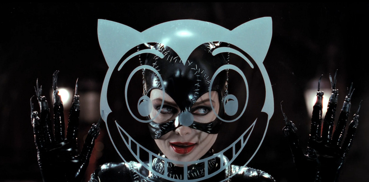 Catwoman (Michelle Pfeiffer) peers through a window past a cat-face decal in Batman Returns