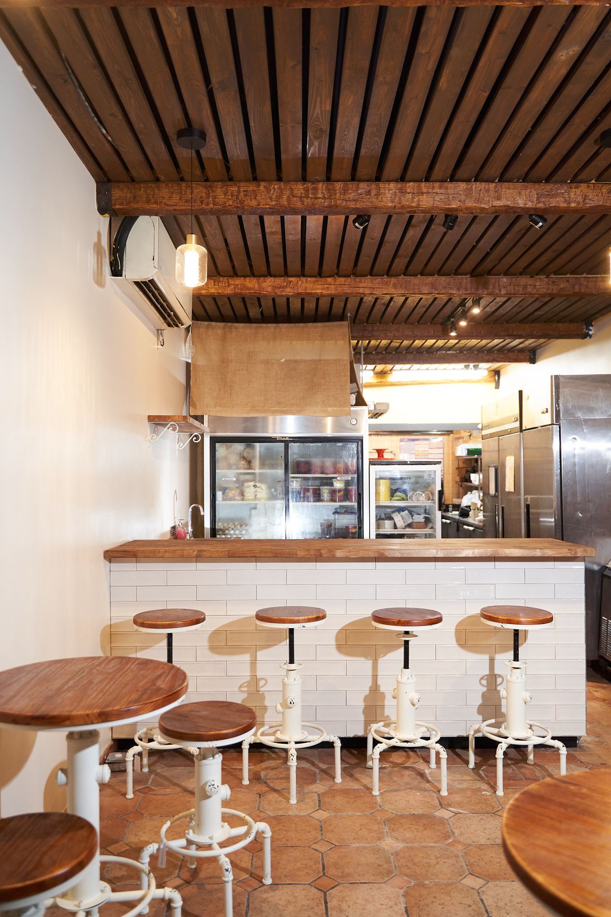 An interior view of a restaurant with a wood-topped counter and stools against a white brick bar.