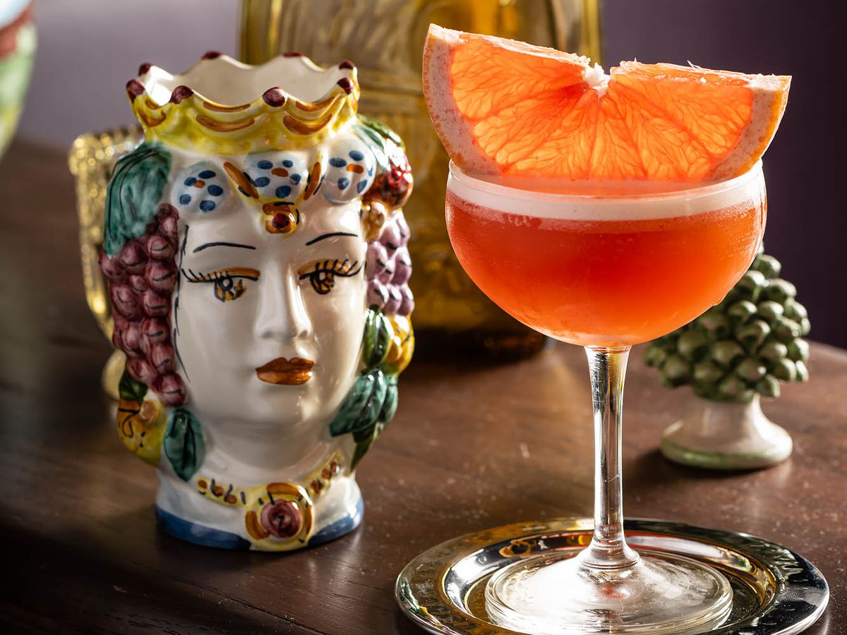 An orange-colored cocktail with a grapefruit slice next to a ceramic doll at Donna’s restaurant.
