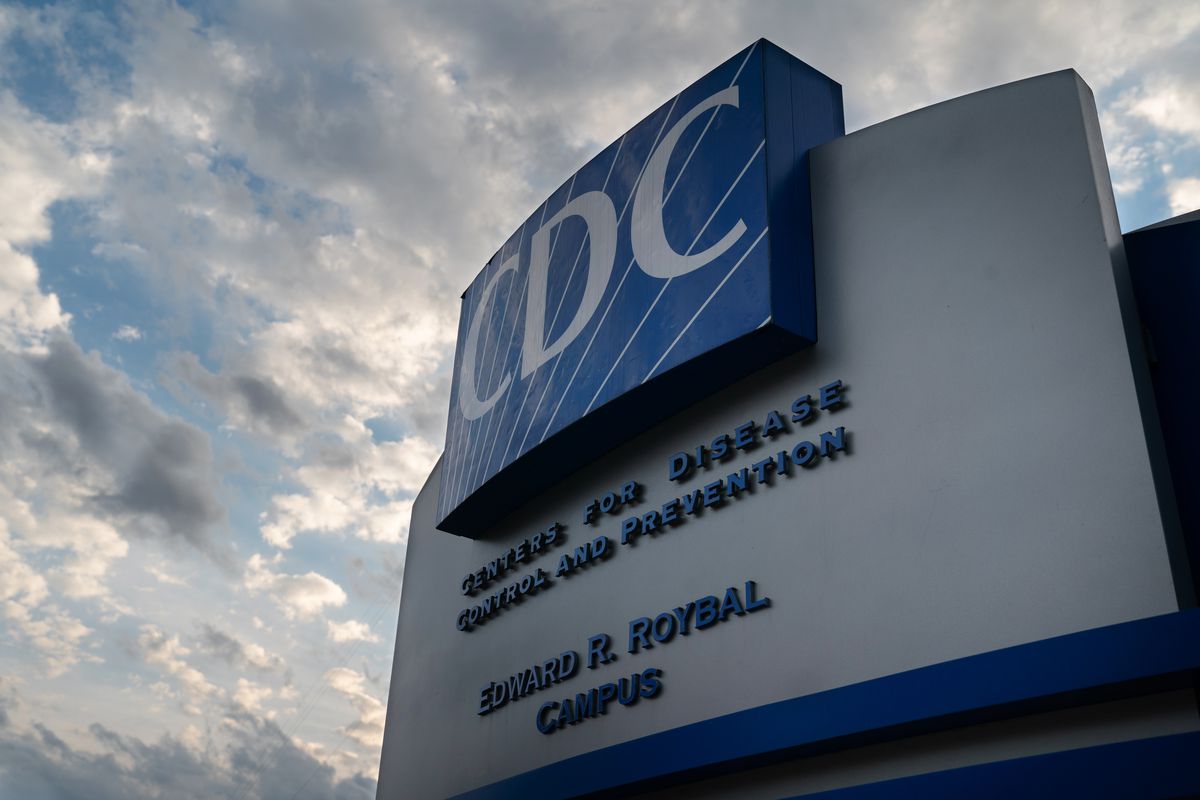 A blue sign reading “CDC” at the CDC headquarters building in Atlanta, Georgia, on a cloudy day.