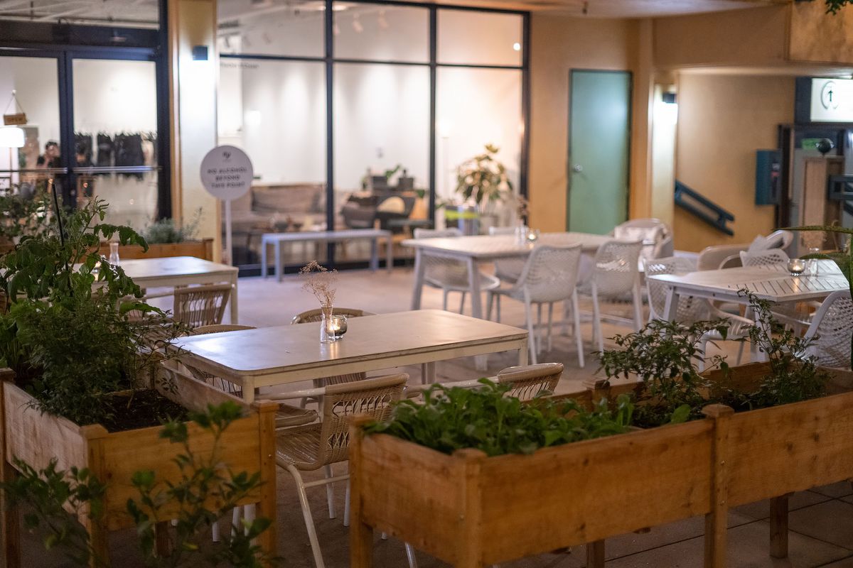 White tables and chairs surrounded by brown raised box planters filled with green plants.