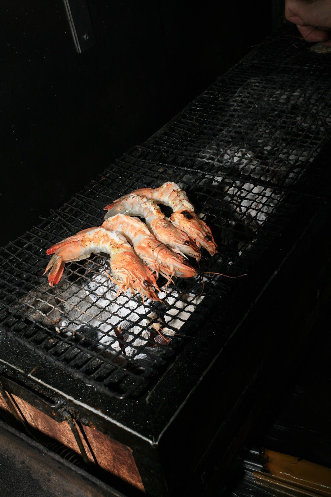 Four prawns, mid-cook so turning a gentle orange, sit over coals on the grill