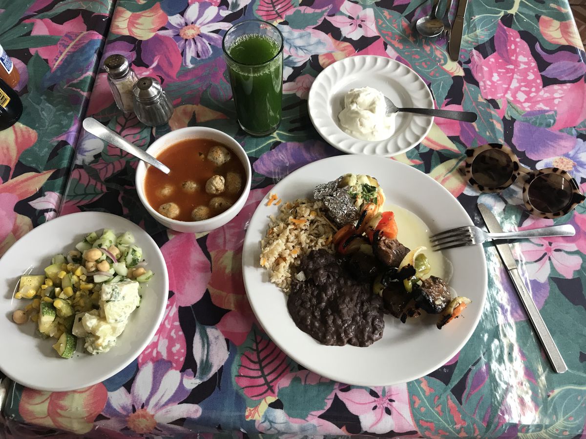 Dishes including a skewer, pilaf, “meatballs” in soup, and salad on a brightly patterned table.