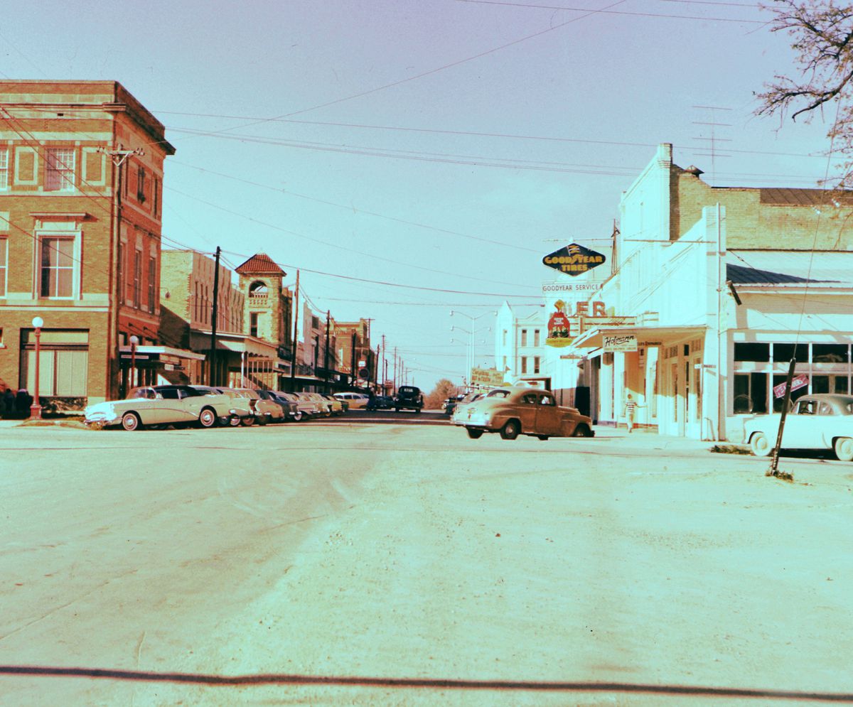 An older photo of a street with buildings and older cars. 