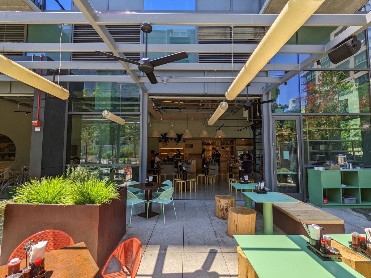 A semi-shaded restaurant patio at daytime, with green and orange seats.