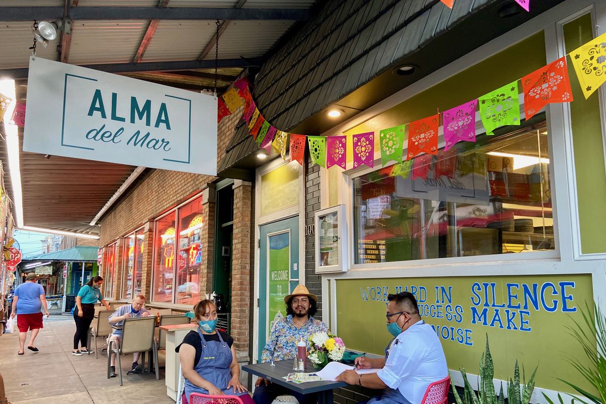 three people at table outside restaurant with sign that says alma del mar