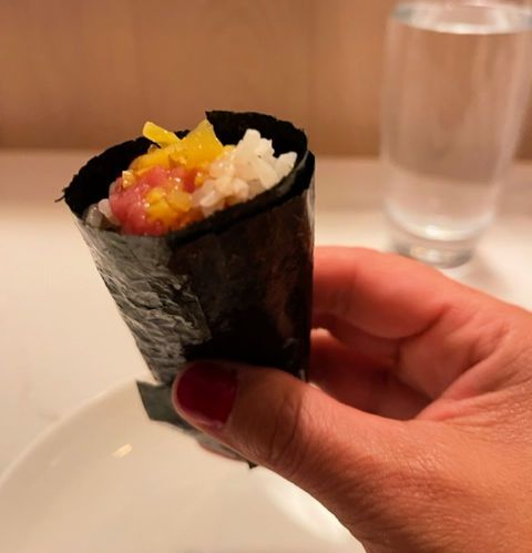 A hand holds a well-made sushi handroll.