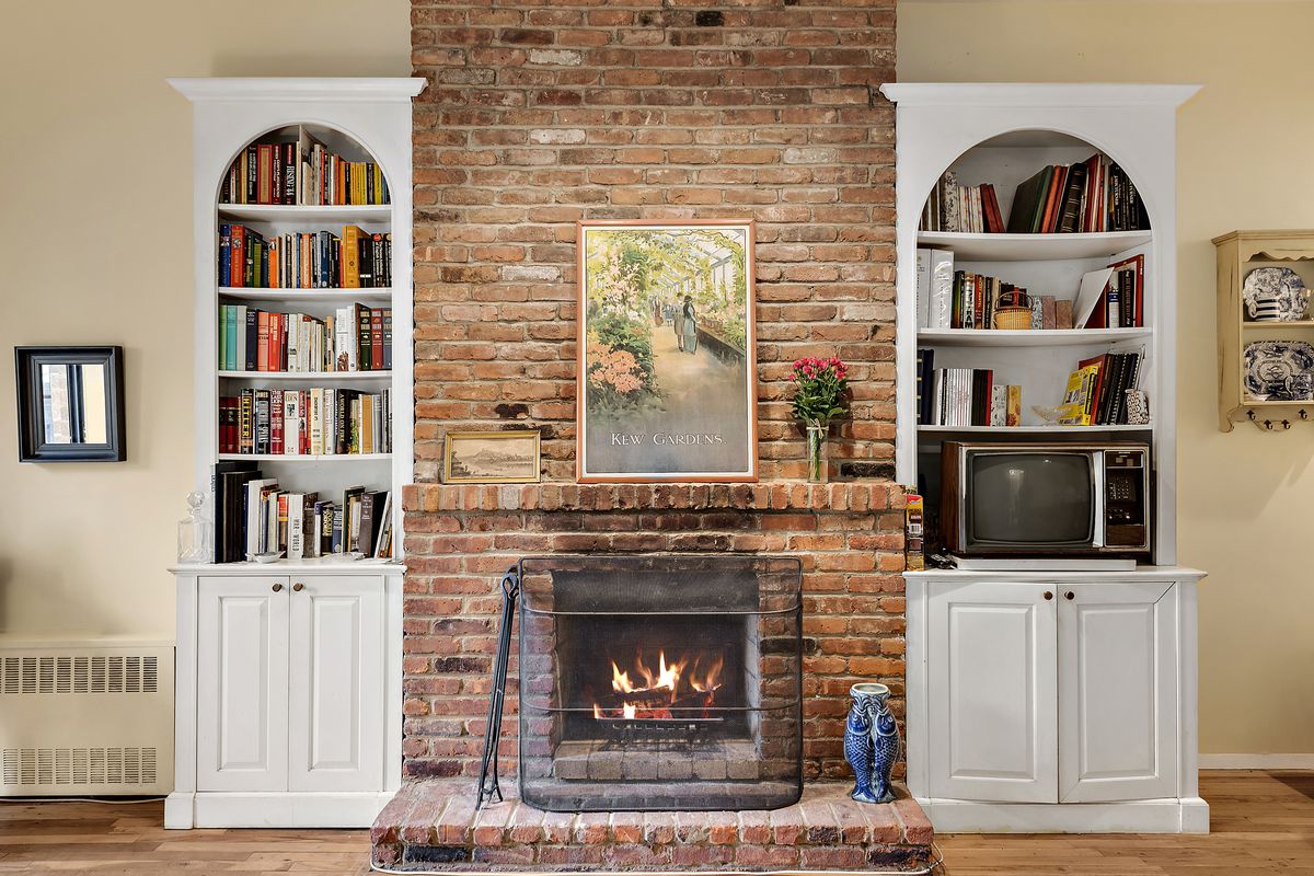 A wood-burning fireplace surrounded by a brick wall and two white built-in bookshelves.