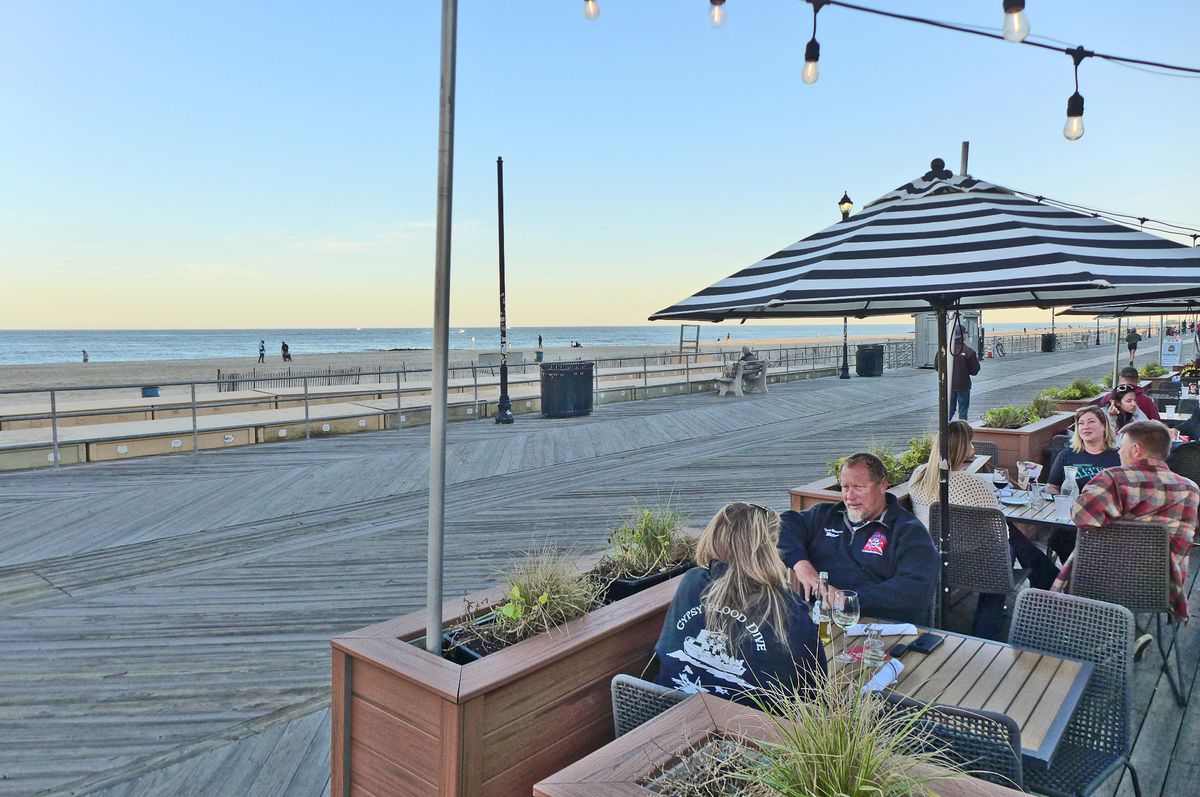 On the right a boardwalk cafe with a few patrons seated, on the left the broad ocean is a thin blue line.
