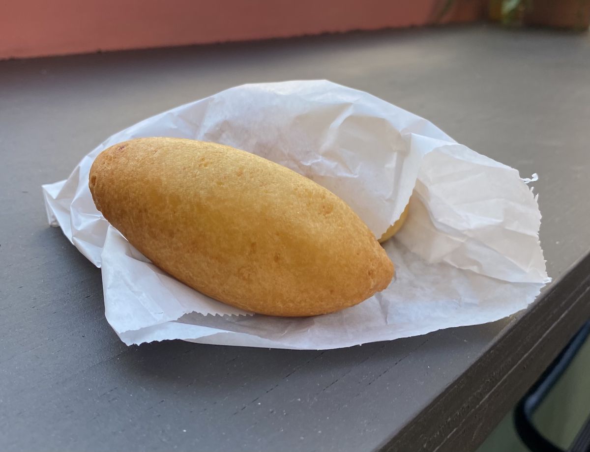A yellow, oblong, guava-stuffed cheese fritter sits on a wax paper on a counter