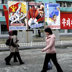 North Koreans walk past posters reading "Forward to the ultimate victory under the leadership of the great party!" left, "not with words but with arms," center, and "Higher, faster," right, on Tuesday, March 19, 2013, on a street in Phyongchon District in Pyongyang, North Korea. The banner partially shown at right reads in its entirety "Let’s strengthen and enhance our party as the party of Kim Il Sung and Kim Jong Il!"