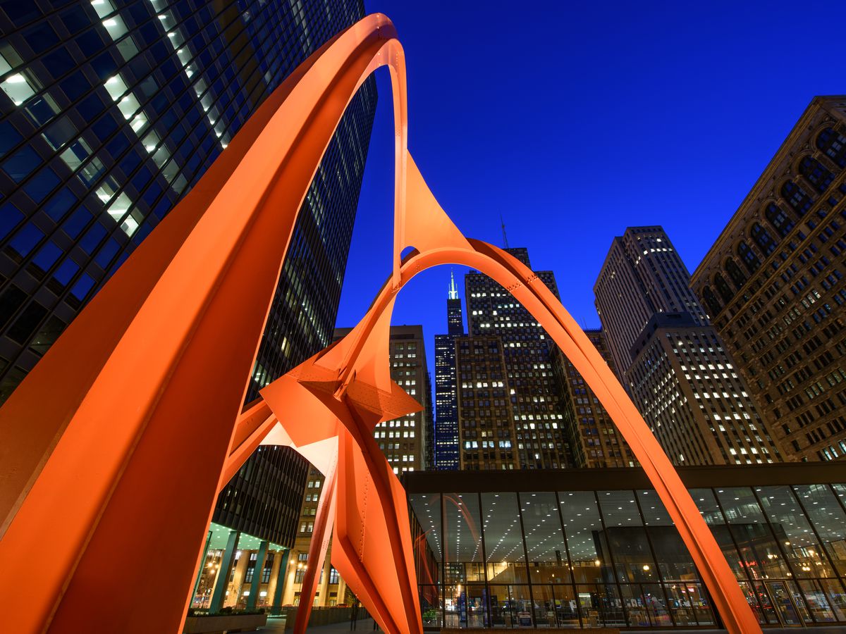 A public work of art in Chicago which is a tall curved orange metal structure near city buildings.