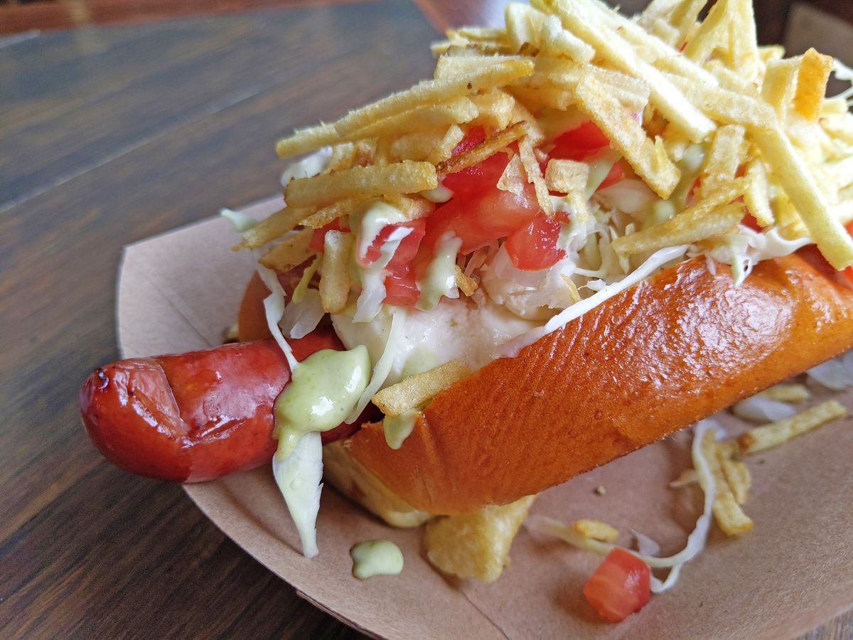 A hot dog covered with toppings and bristling with potato sticks.