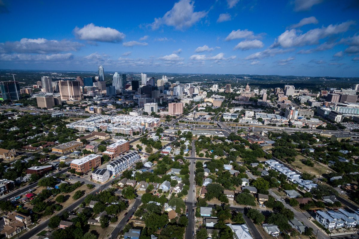 An aerial view of the city of Austin. There are neighborhood streets with houses and a more dense center with skyscrapers and larger buildings. 