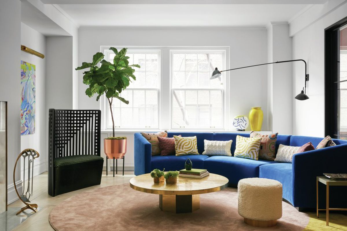 A living area with a blue couch, table, chairs, plants, and large windows letting in natural light.
