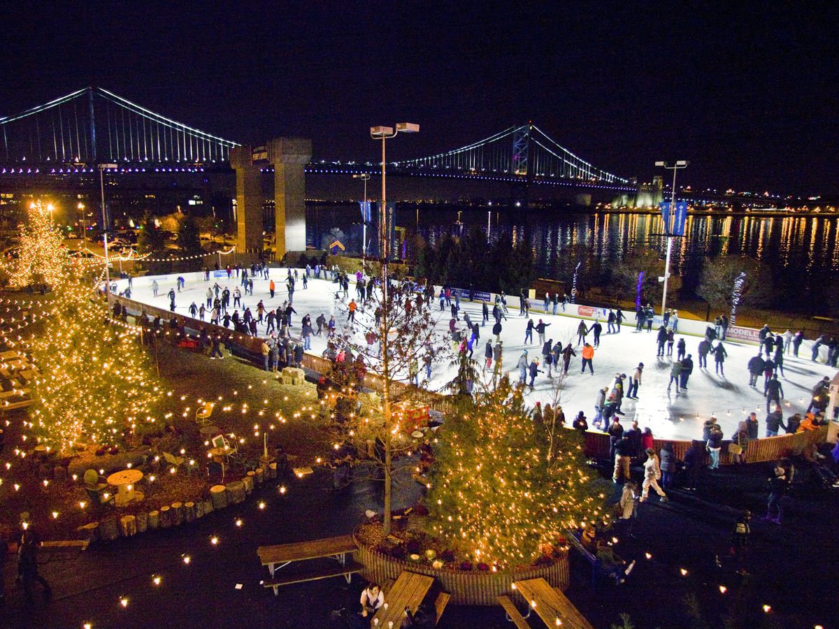An aerial view of Blue Cross RiverRink in Philadelphia. There are many people skating on the ice. In the distance is a bridge. 