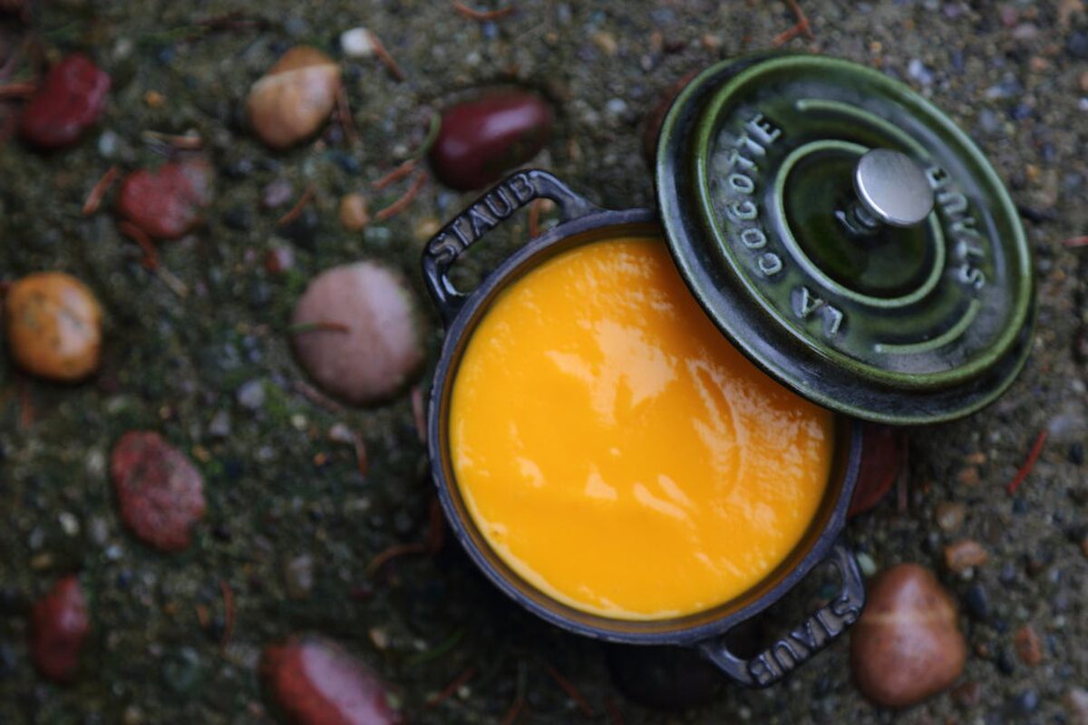 A small black pot filled with creamy carrot soup on a stone-covered counter