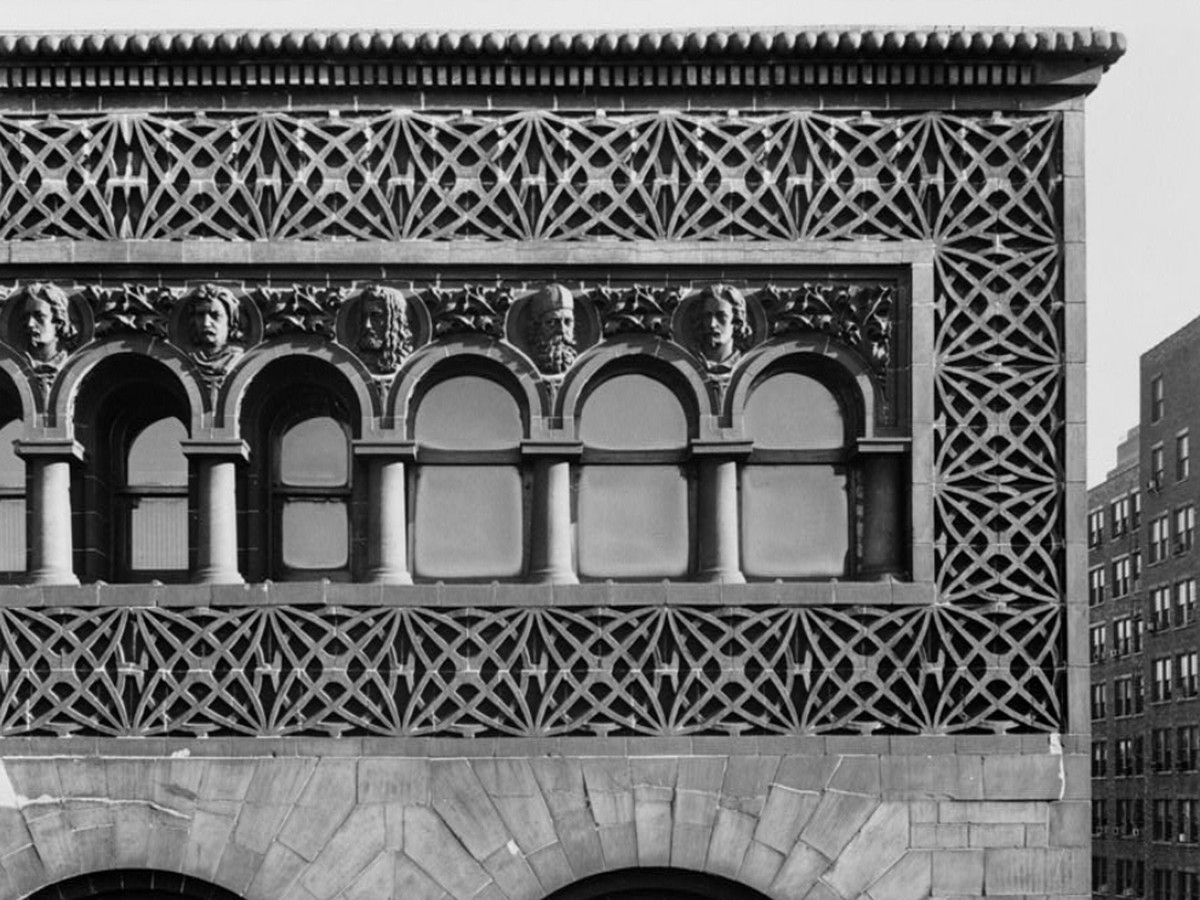 A black and white photograph showing detailed stonework around arched windows with carved busts between each column.