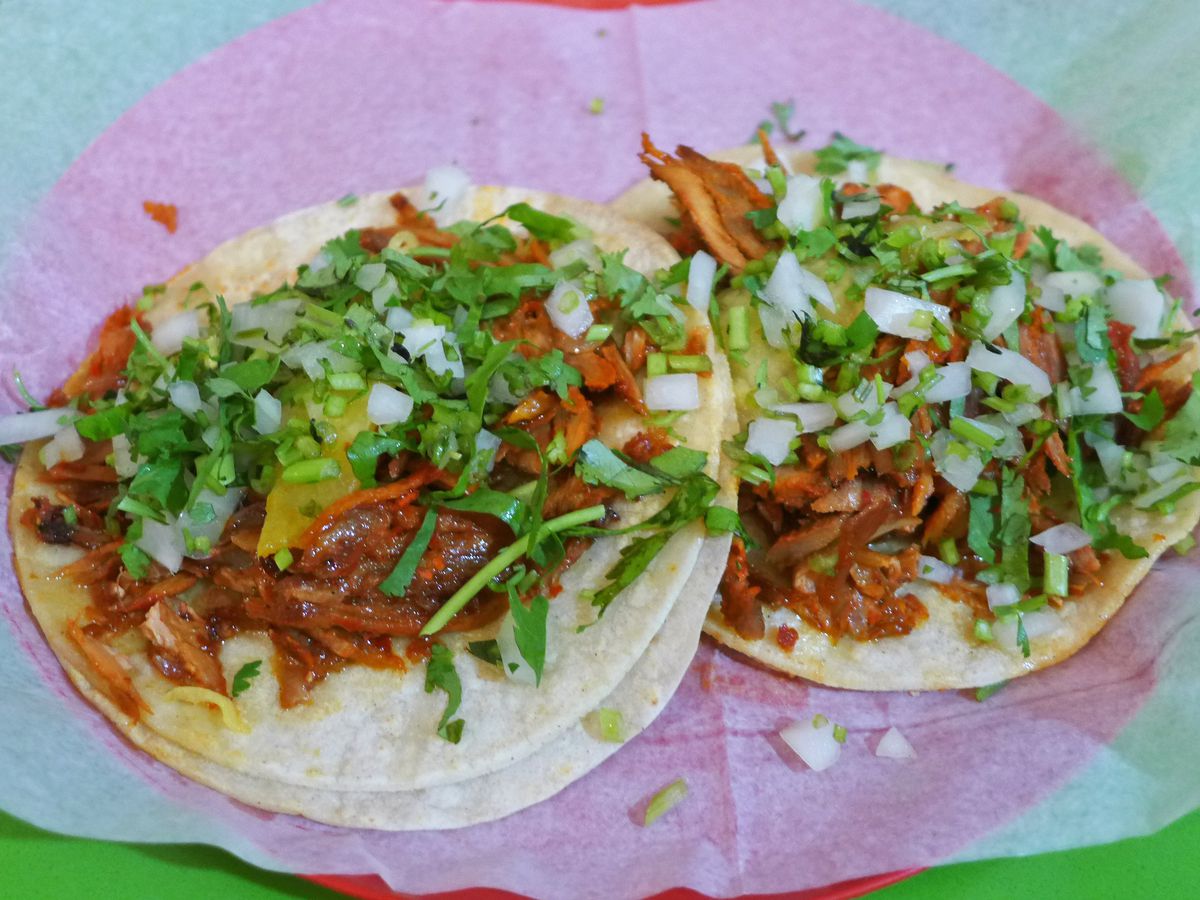 Two tacos spread flat with meat, onions, cilantro, and red salsa.
