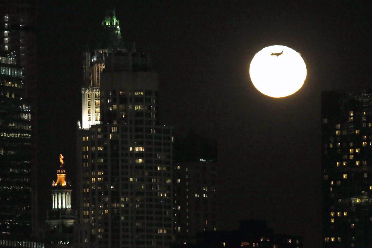 An airplane flies past the rising moon in its waning gibbous stage as viewed from Jersey City, N.J., Thursday, Feb. 5, 2015. The statue known as Civic Fame, bottom left, which stands atop of the Manhattan Municipal Building in New York, is also visible. (