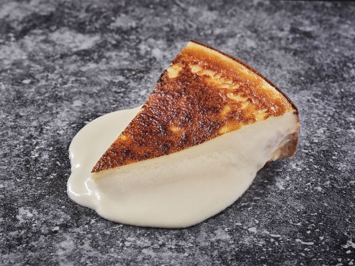 A slice of cheesecake in a pool of white sauce. 