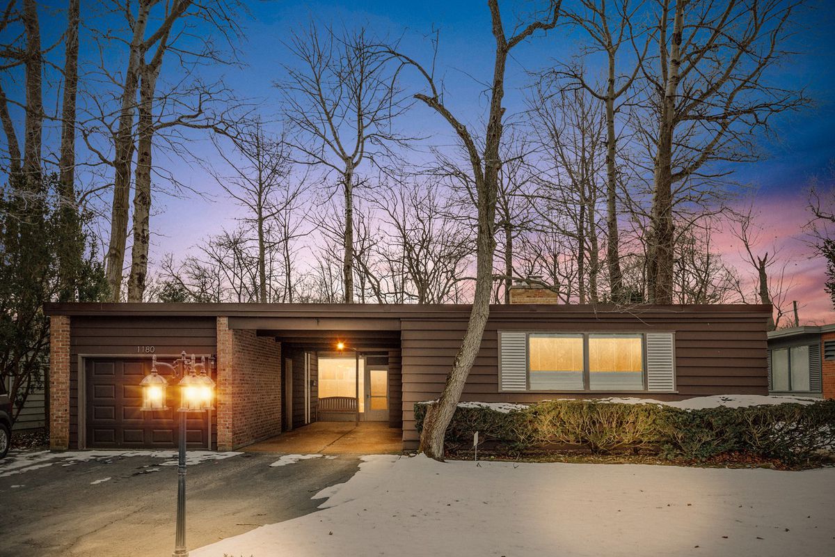 A single-level ranch home with a flat roofline surrounded by trees. 