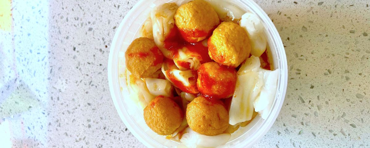 A container of rice noodles with curry fishballs.