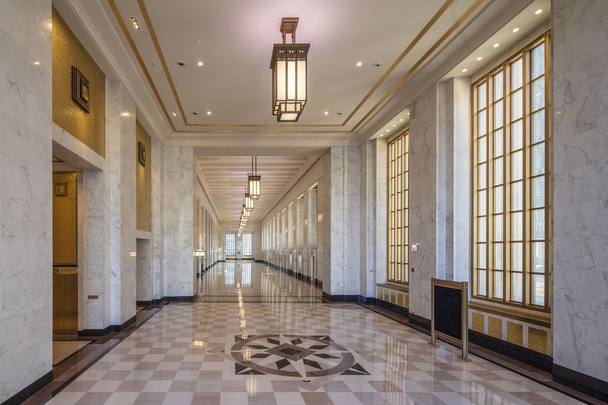 A long marble-clad hall with high ceilings, a checker pattern stone floors, and oversized bronze-framed windows.