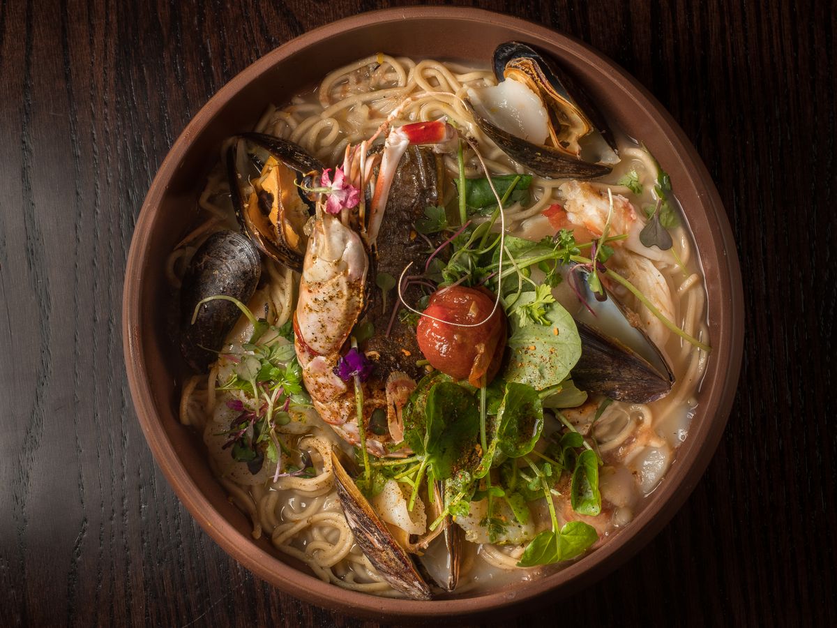 A closeup of an earthenware bowl filled with ramen, broth, and topped with half a prawn