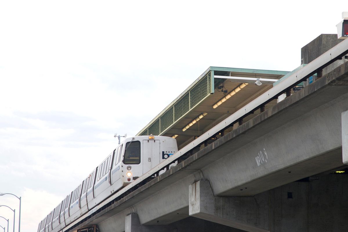 A BART train pulling into a station on elevated tracks, photographed from the ground.