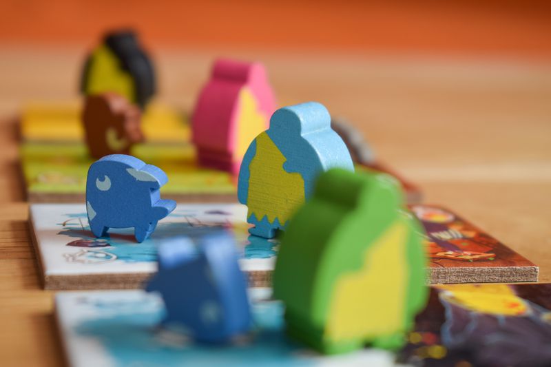 A fish and a cave person meeple, in blue, stand on a set of Kingdomino Origins tiles ready to be played to the table.