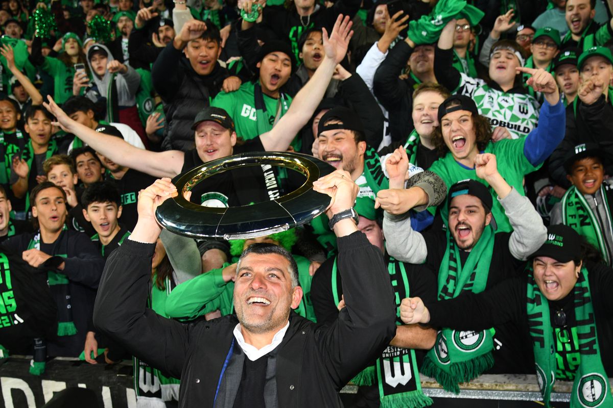 A man holds up a UFO shaped trophy in front of a crowd of supporters