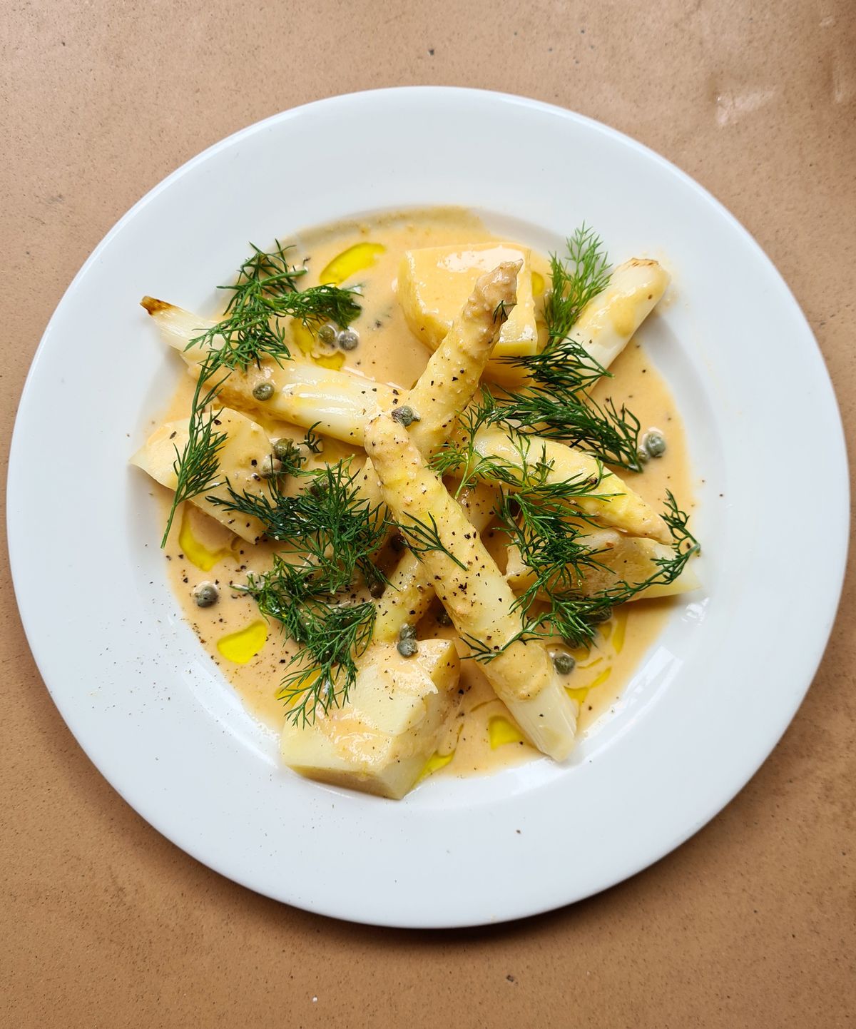One of the best dishes in London restaurants: a plate of white asparagus in a brown crab butter, scattered with fennel fronds, capers, and dill