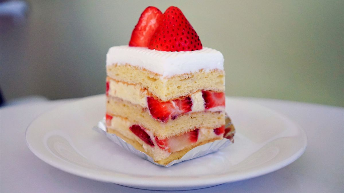 A slice of cake with layers of strawberries and cream and a strawberry on top.