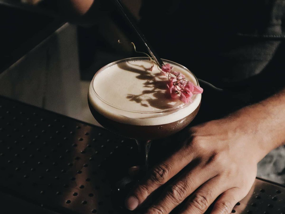 A bartender lays a floral garnish on a cocktail. 