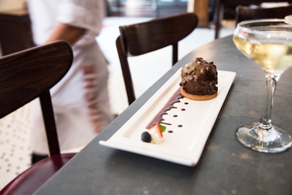This is a picture of a chocolate dessert on a rectangular white plate. A waiter is walking by in the background.