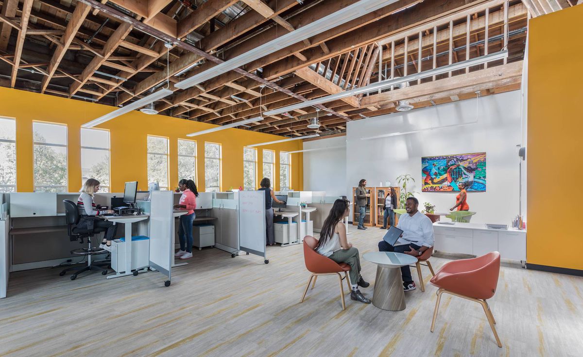 An office with yellow walls, exposed wood beams, large windows, and skylights
